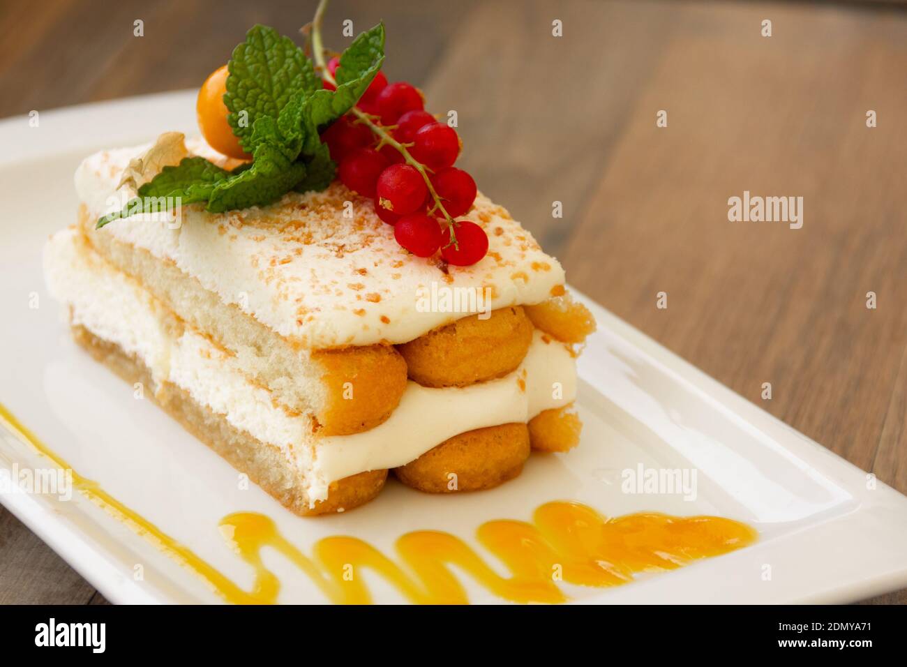 Succulent lady fingers cake with cream, red berries and glazed on top of white plate with peach jam decoration. Sweet dessert, gourmet presentation Stock Photo