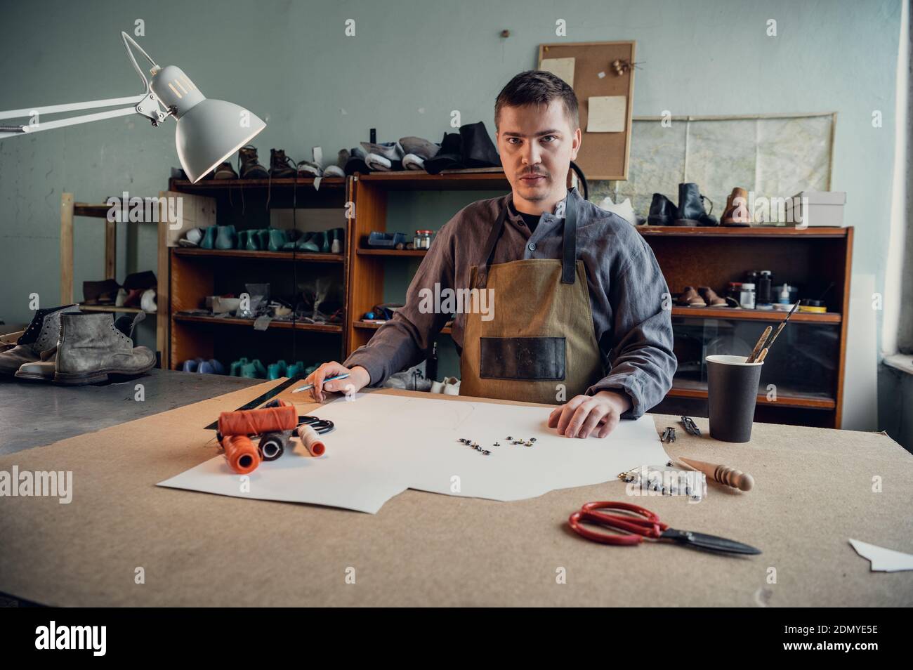 In a family shoe shop a young apprentice works with paper to create a pattern for shoes. Stock Photo