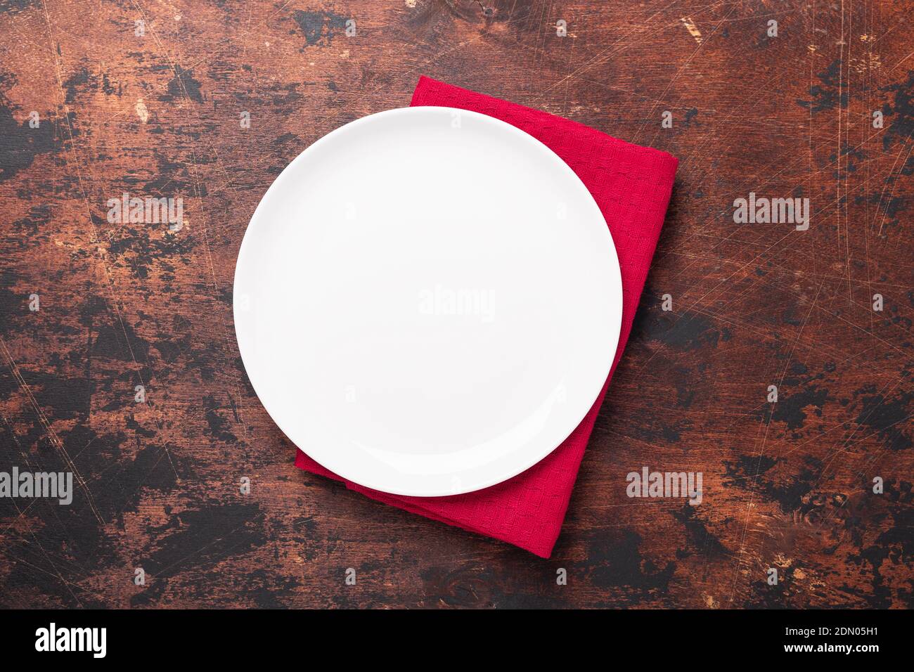 Empty ceramic white plate and red linen napkin on brown wooden background Copy space Top view - Image Stock Photo