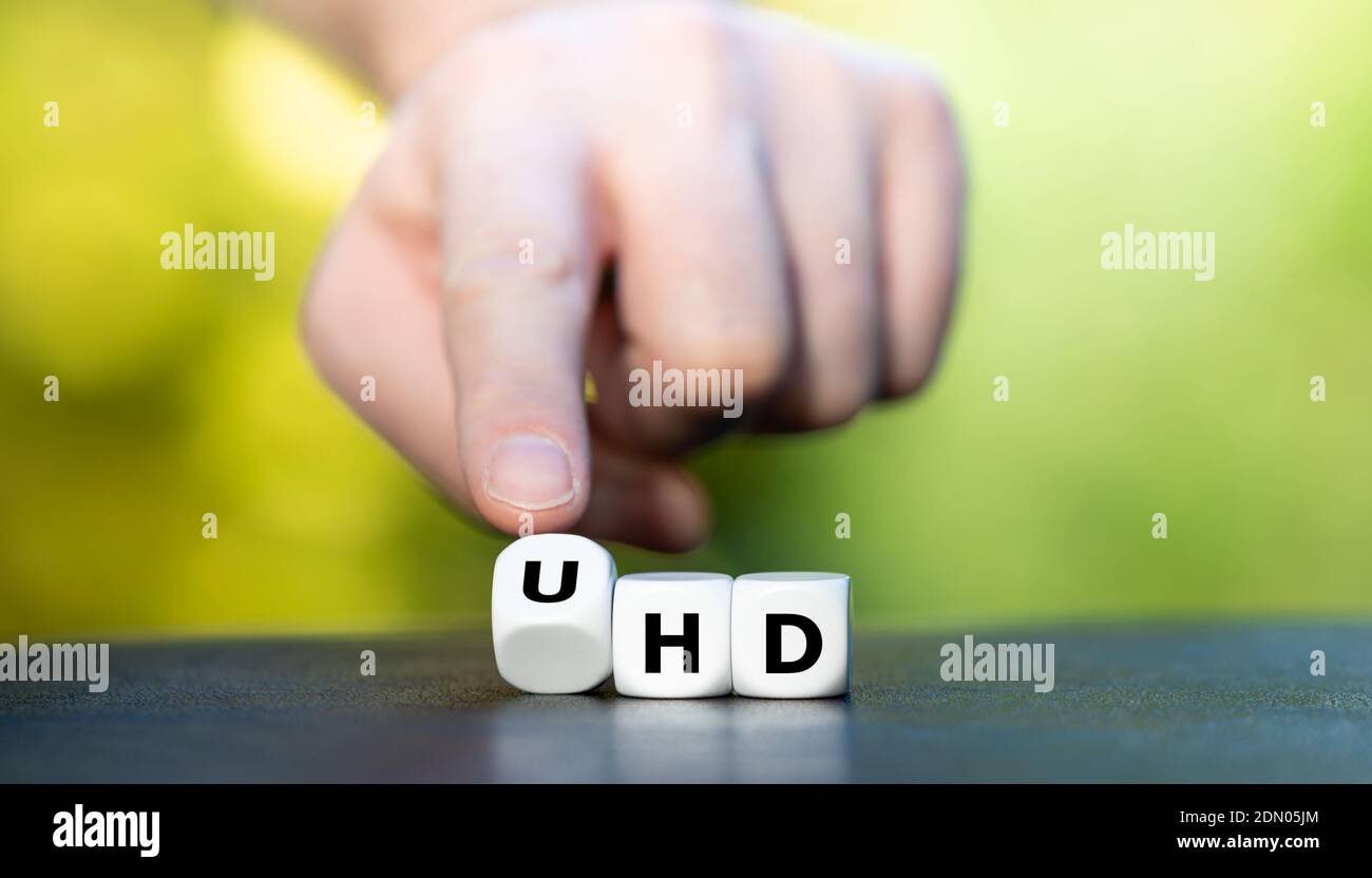 Symbol for a ultra high definition (UHD) television. Hand turns dice and changes the expression 'HD' to 'UHD'. Stock Photo