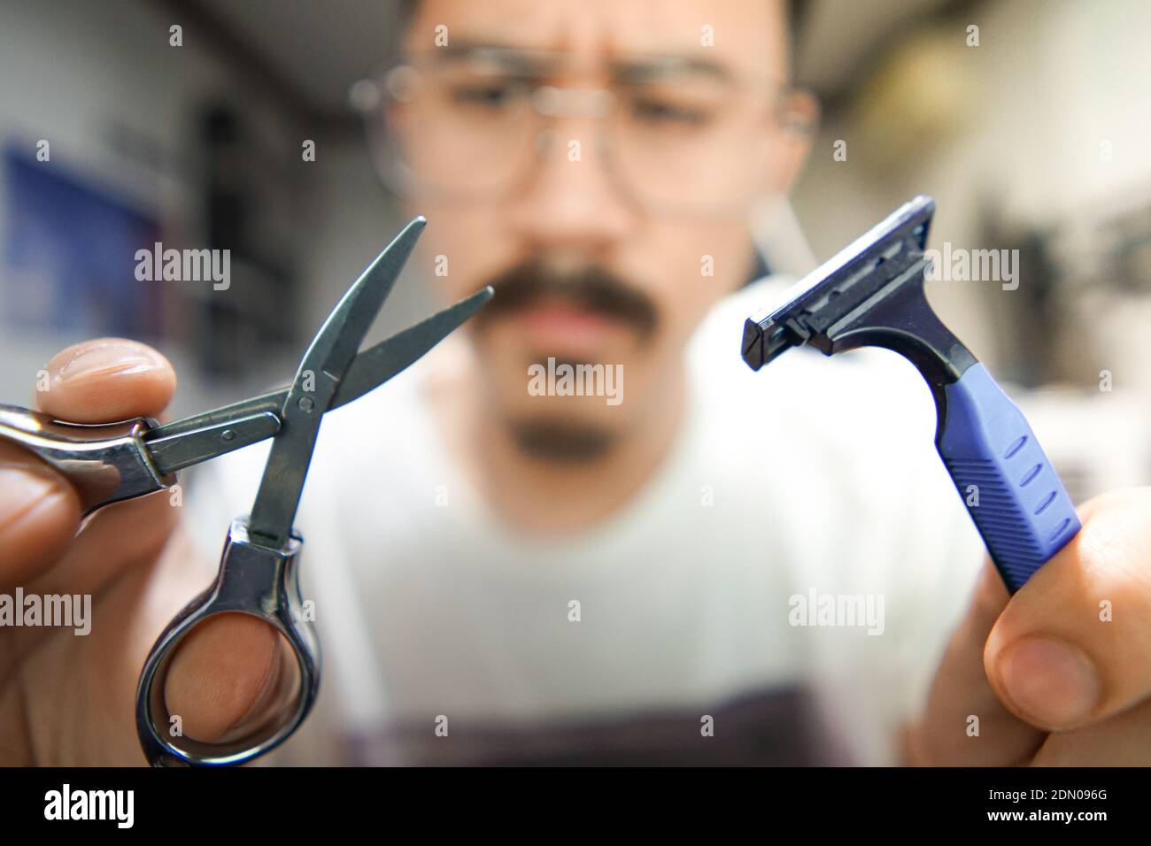 Man Wearing Eyeglasses Holding Scissors And Razor At Home Stock Photo
