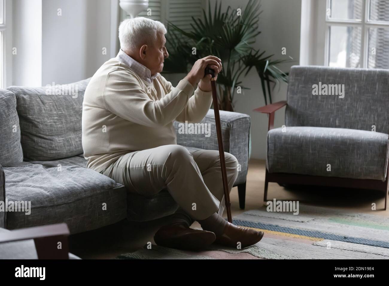 Thoughtful mature male resting on sofa leaning on walking stick Stock Photo
