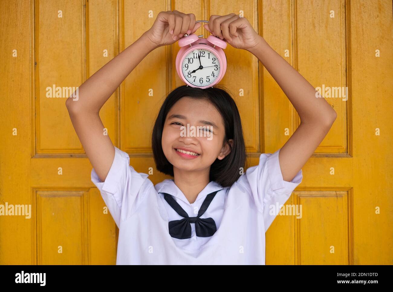 Portrait Of Smiling Teenage Girl Holding Alarm Clock On Head Against Door Stock Photo Alamy