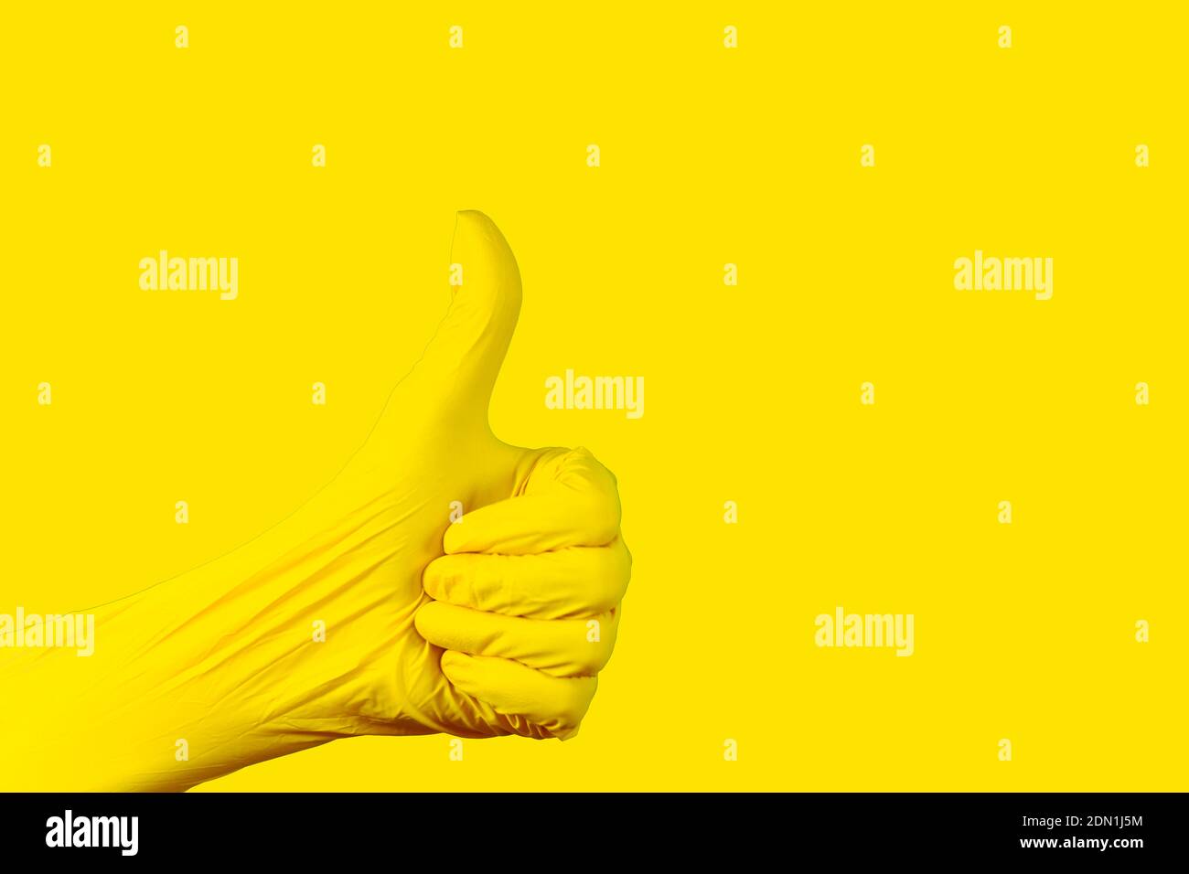 Gesture of a hand thumb up in a nitrile yellow Illuminating glove against a uniform background of the same color. Stock Photo