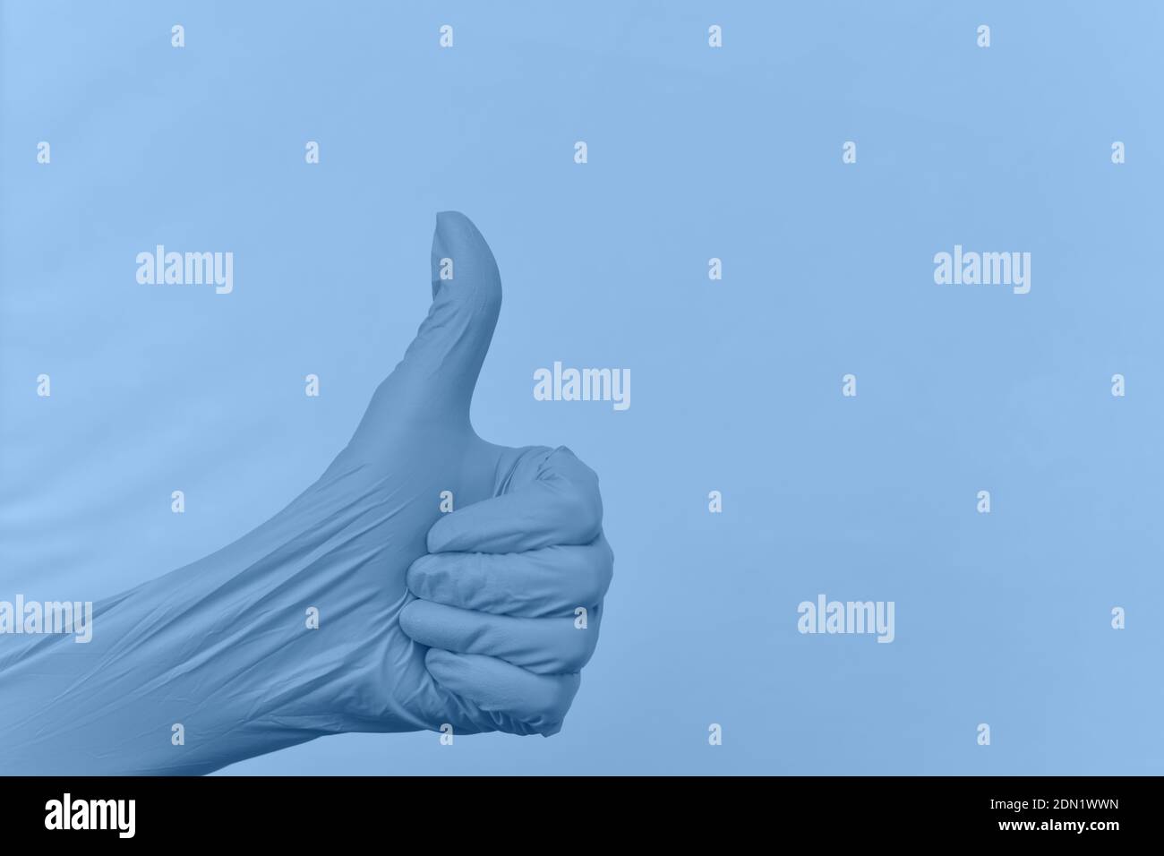 Gesture of a hand thumb up in a rubber glove color placid blue against a raised tinted background with folds. Stock Photo