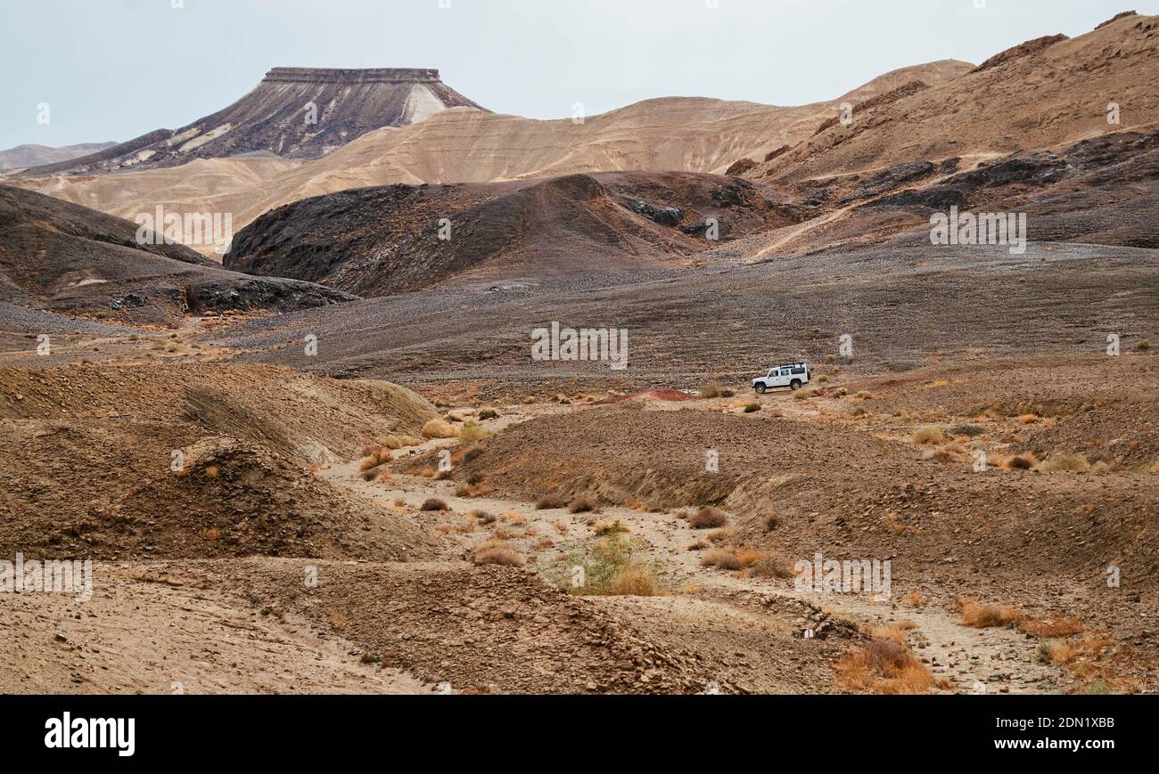 a white off road vehicle in the gevanim stream bed with a hiking trail in the foreground in the makhtesh ramon crater in israel with mount katum Stock Photo