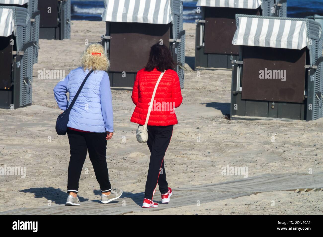 A pair of women walking away from the beach among wicker beach chairs in the late summer sunshine, Germany Stock Photo