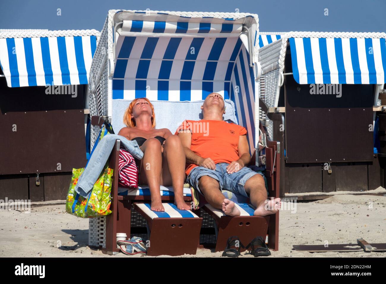 Couple sunbathing on beach chairs enjoying the sun, sheltered from the wind, Germany Baltic sea strandkorb Stock Photo