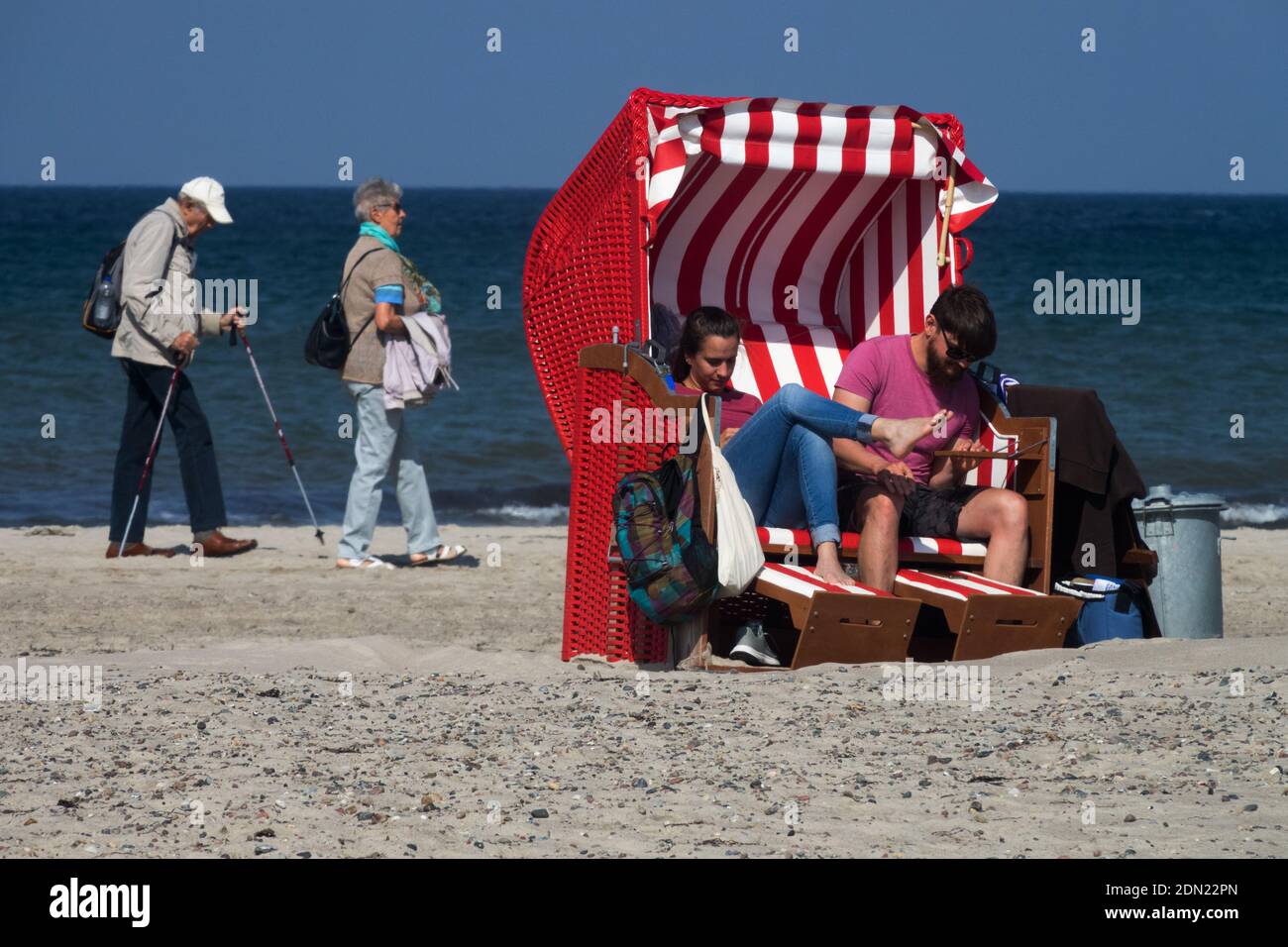A young couple in a beach chair and a senior couple walking on a beach Germany Baltic Sea shore, a young couple old couple Stock Photo