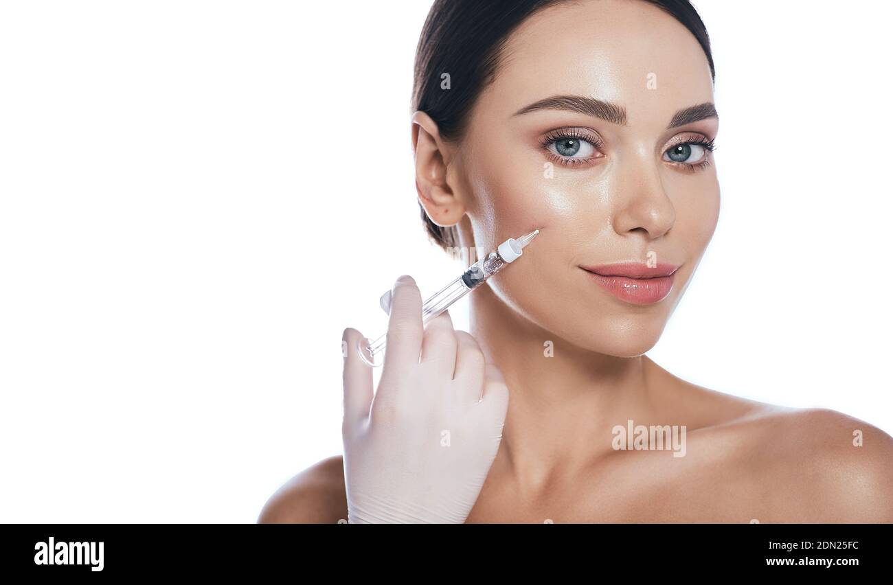 Beautician doing injections dermal fillers into female cheeks for a