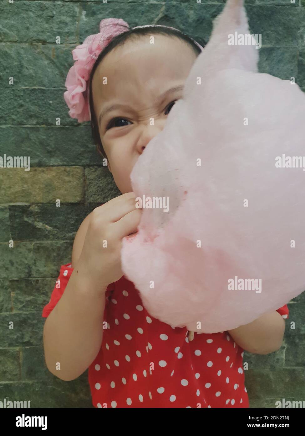 Cute Girl Eating Cotton Candy While Standing Against Stone Wall Stock