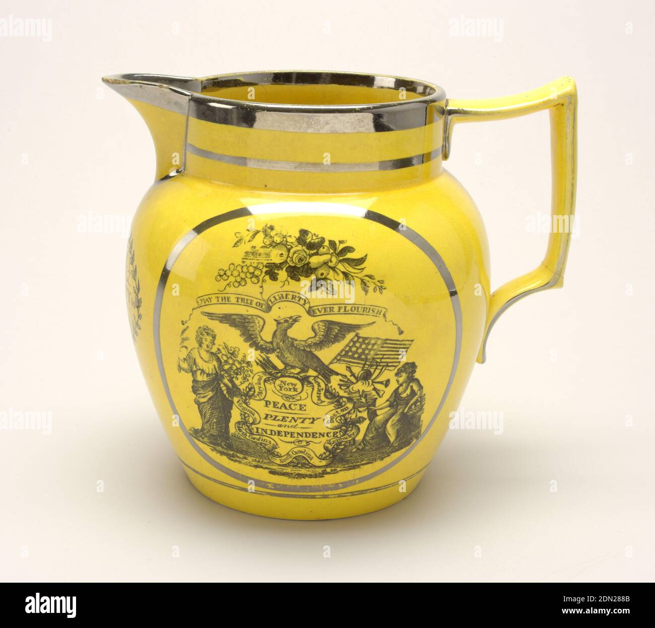 Pitcher, Glazed earthenware, silver resist, transfer printed and luster decoration, Tapering bulbous form with circular mouth and deep spout; large, squared loop handle. Yellow glaze ground with silver luster bands and black transfer-printed decoration: on one side, medalion with message, 'May The Tree of Liberty Ever Flourish,' accompanied by various symbols and attributes; on the opposite side, cartouche with message 'Success to the United States of America,' accompanied by symbols and attributes, and surmounting ribbon with 'E Pluribus Unum'; under spout, 'Peace and Prosperity to America Stock Photo
