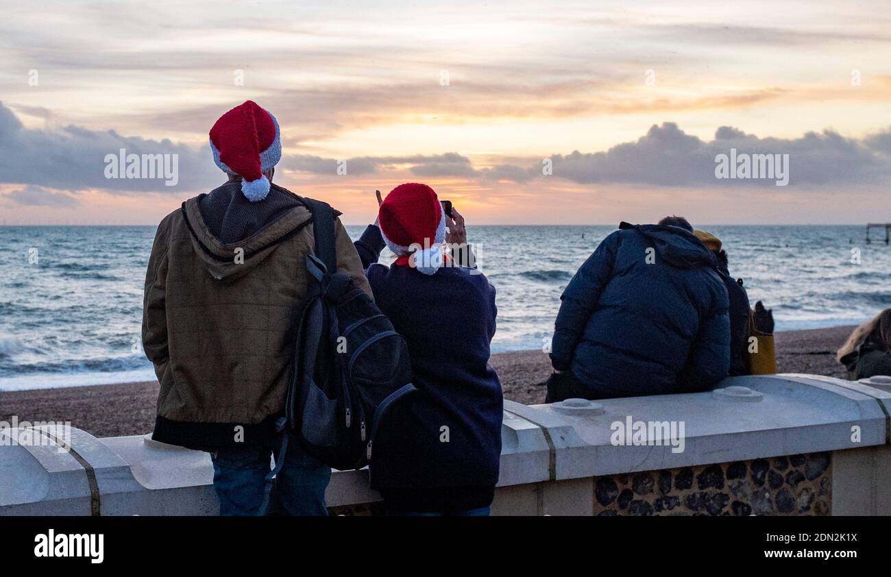 Brighton UK 17th December 2020 - A couple in Santa hats make the most of the sunset on Brighton seafront at the end of a bright day on the South Coast . The city of Brighton and Hove has been kept in coronavirus Tier Two restrictions in England after an announcement  earlier today by the Health Secretary Matt Hancock : Credit Simon Dack / Alamy Live News Stock Photo