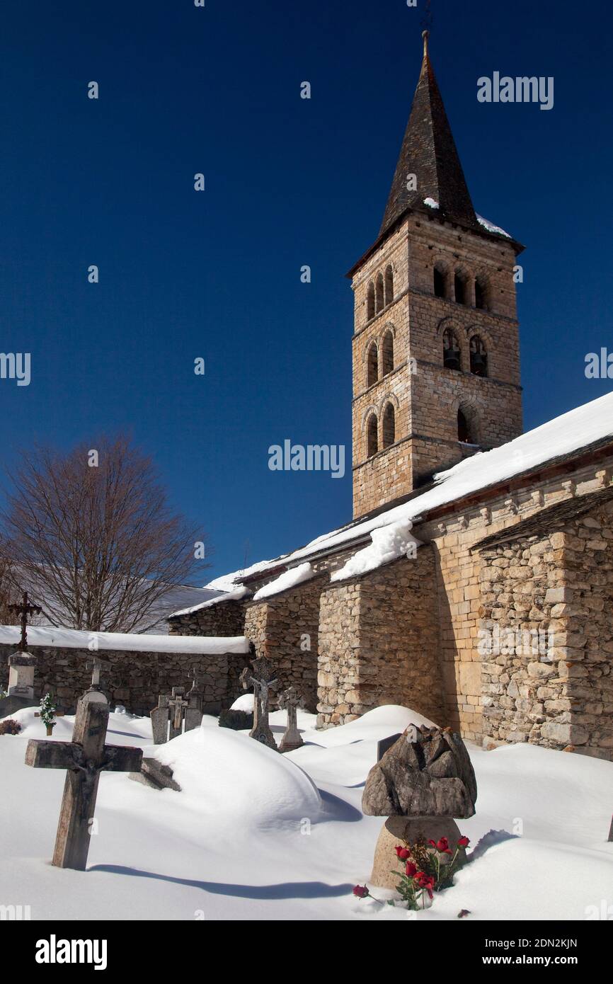 Vertical view of the graveyard and bell tower of the Romanesque Santa María church covered by snow, Artíes, Vall d’Aran, Lleida, Catalonia, Spain Stock Photo