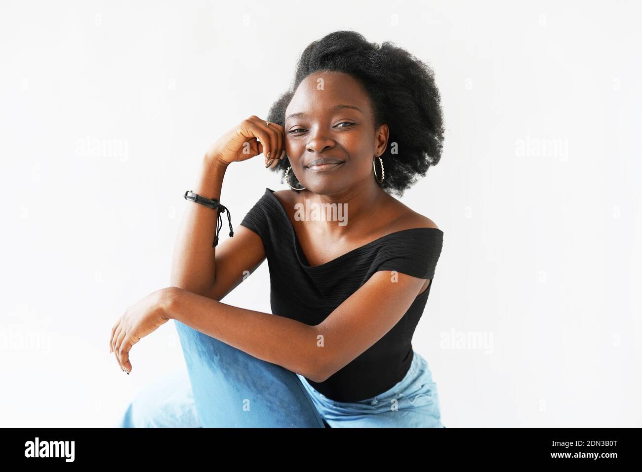 Portrait of a cheerful Afroamerican young woman sitting and looking at the camera on white background Stock Photo
