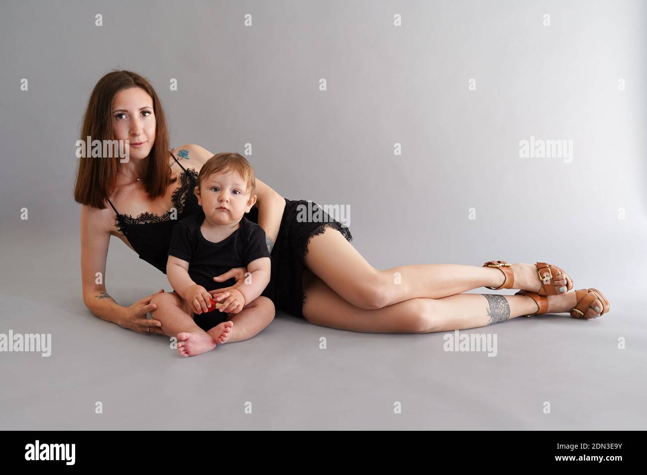 Young beautiful mother in little black dress lying with her son on the floor and taking a foto in studio Stock Photo
