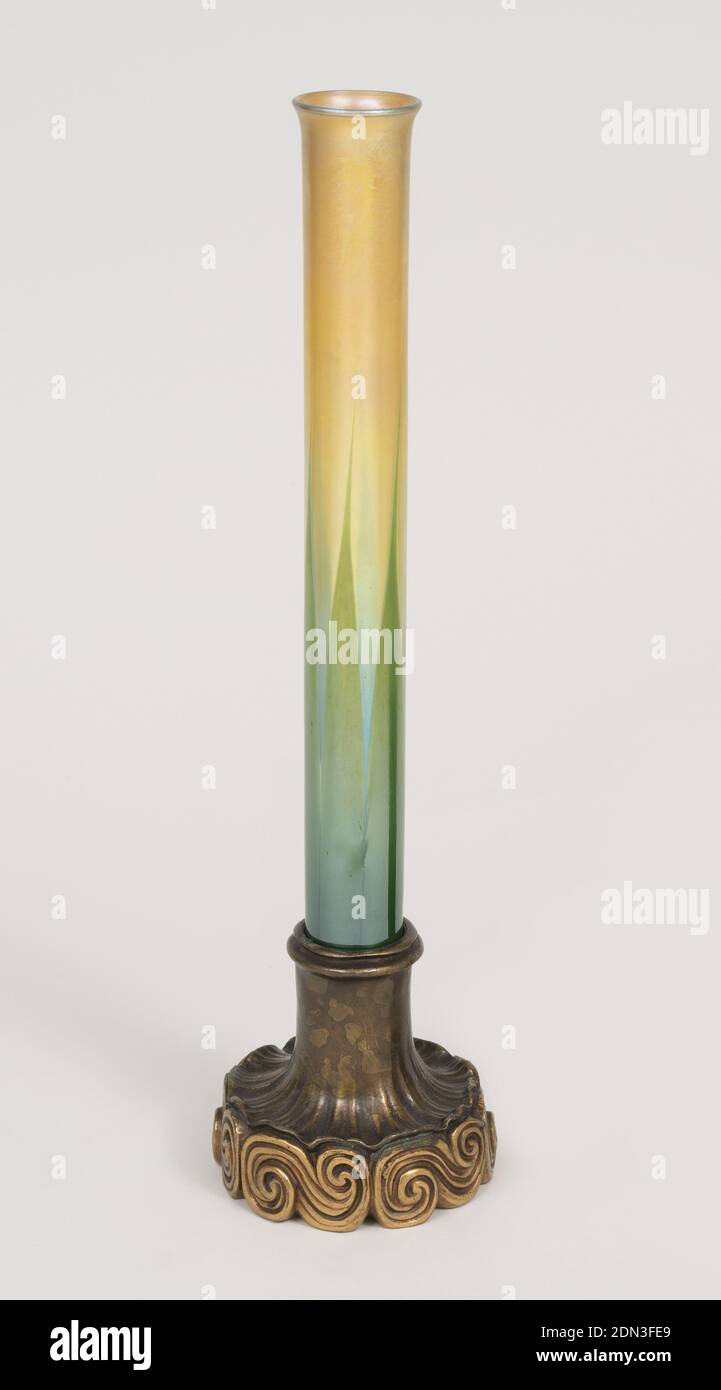 Bud vase, Tiffany Glass and Decorating Company, American, 1892 - 1900, Mold-blown favrile glass, cast bronze, Tall, cylindrical glass vase (a) with slightly flared mouth; dark green leaf motif at bottom eased over gold favrile glass. Vase fits into socket of bronze base (b) patinated at top, inverted trumpet-shaped, ruffled, resting on series of horizontal S-curves picked out with gilding. Three metal 3-pronged holders (c,d,e) to fit into base to hold vase., New York, NY, USA, ca. 1900, glasswares, Decorative Arts, Bud vase Stock Photo