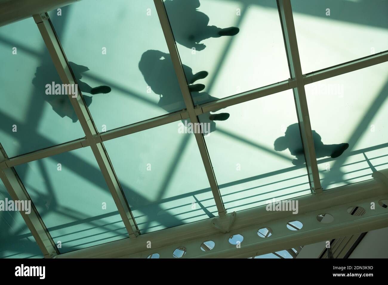 View from underneath at shadow of people walking on a glass bottom walkway in shopping mall, Lisbon, Portugal Stock Photo