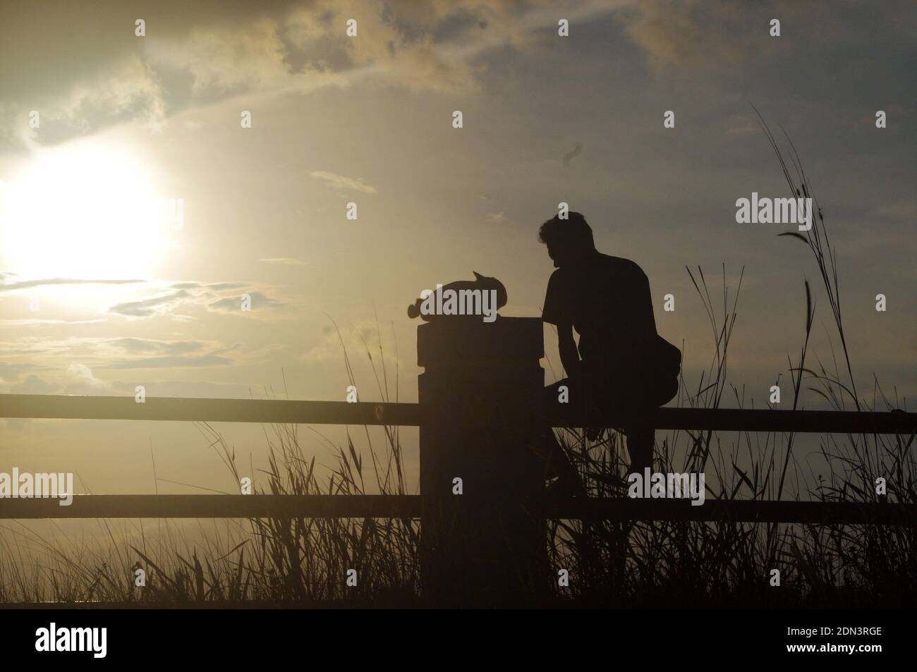 Silhouette Man Sitting On Railing Against Sky During Sunset Stock Photo