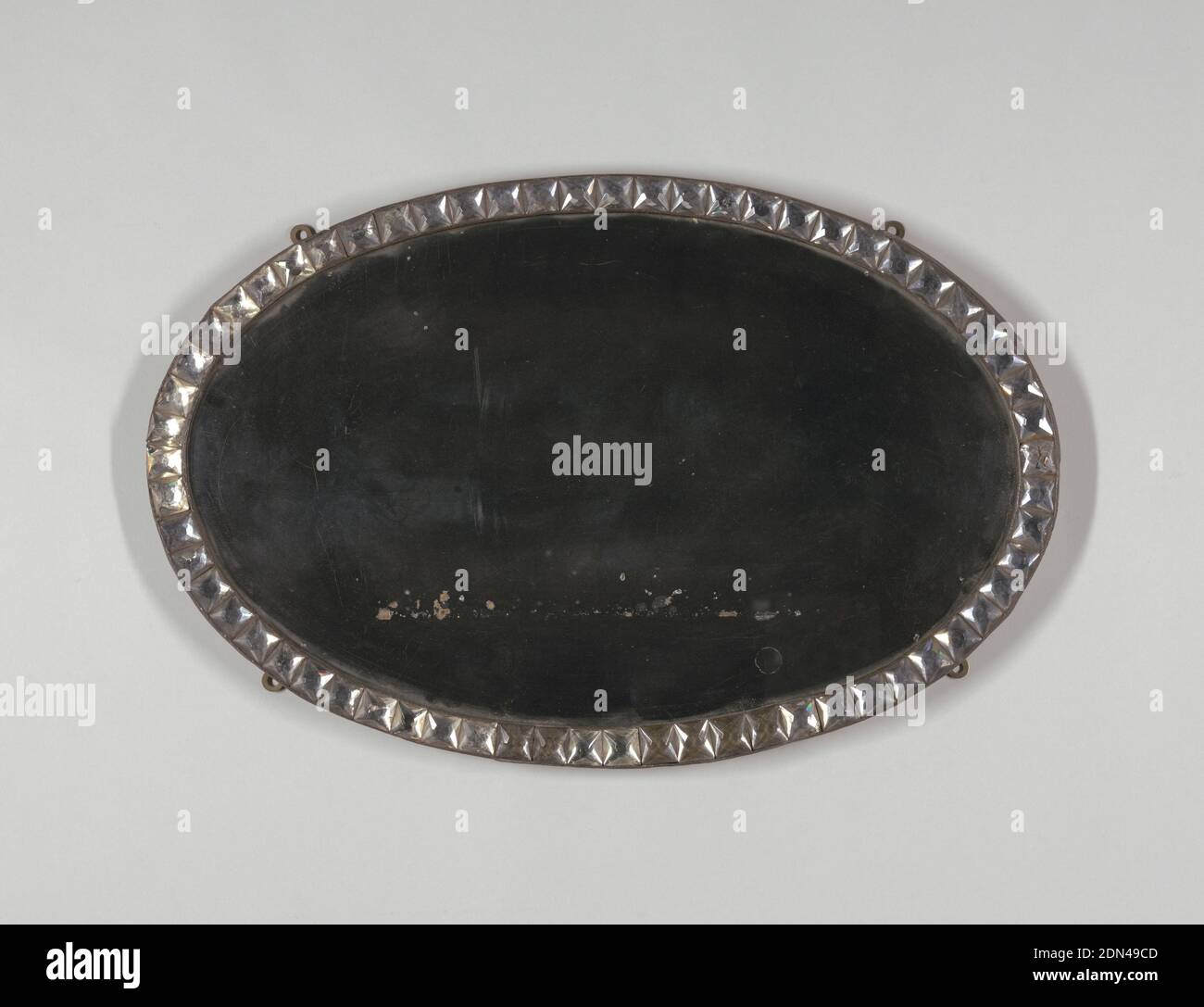 Mirror, Cut glass, mirrored glass, metal, wood, Oval mirror surrounded by oval metal frame with row of square, faceted glass 'jewels'; wood backing; four mounting rings on reverse, allowing vertical or horizontal orientation., Ireland, late 18th–early 19th century, glasswares, Decorative Arts, Mirror Stock Photo