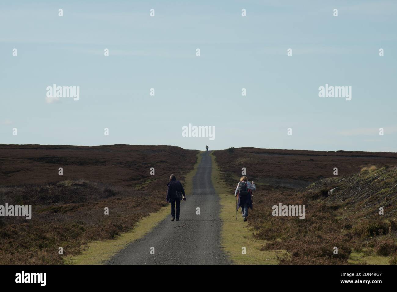 Two female walkers heading along the Waskerly Way moorland path with a single walker outlined on the distant horizon forming a strong triangular shape Stock Photo
