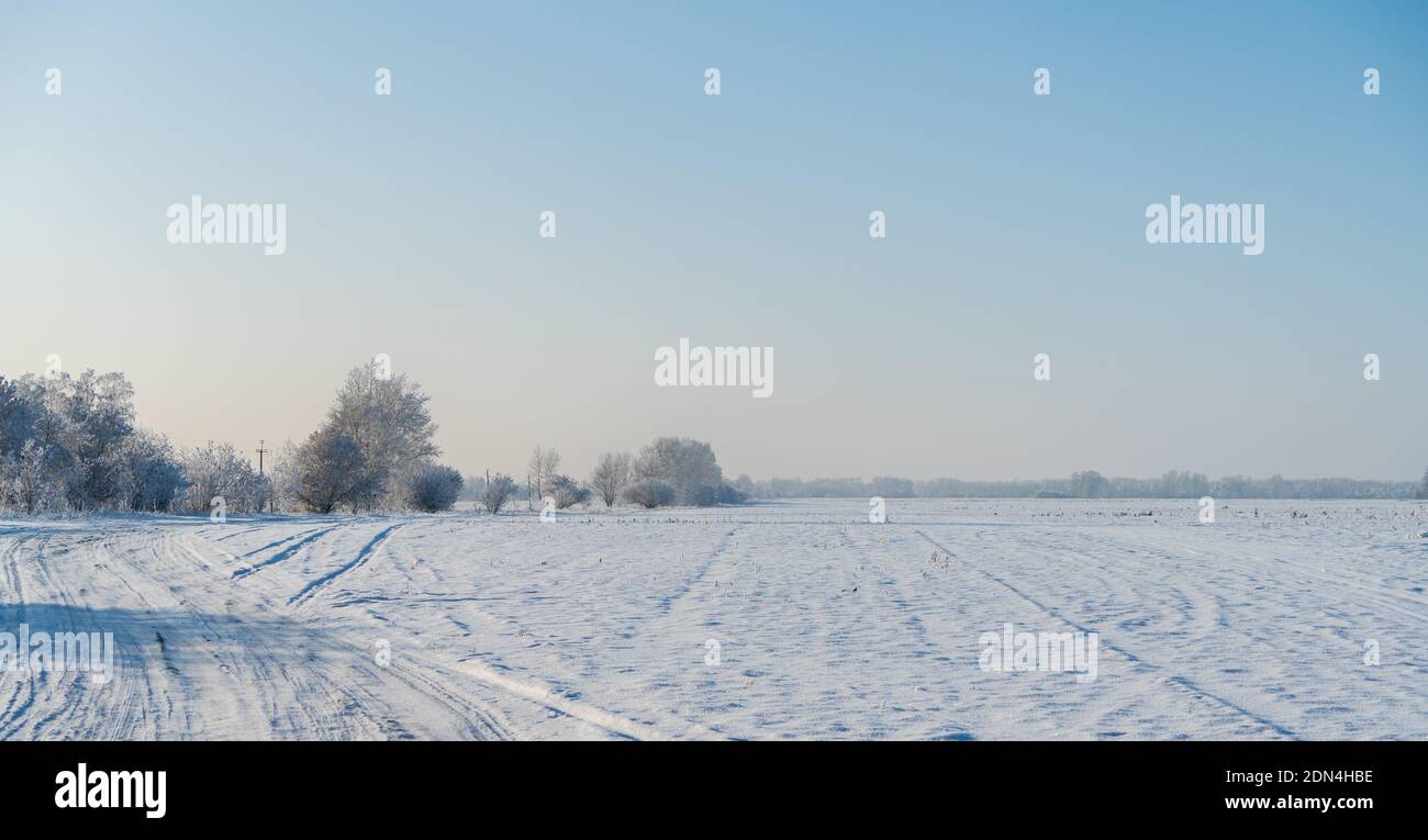 Snow covered winter field with trees and road going through to the ...