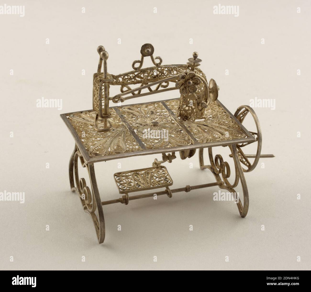 Sewing machine, Silver, Filigree miniature comprising sewing machine form on rectangular table top with decoration in three panels, on scrolled supports. The working parts consist of a treadle, crank, slotted arm, and needle., Italy, mid-19th century, miniatures, Decorative Arts, Miniature, Miniature Stock Photo