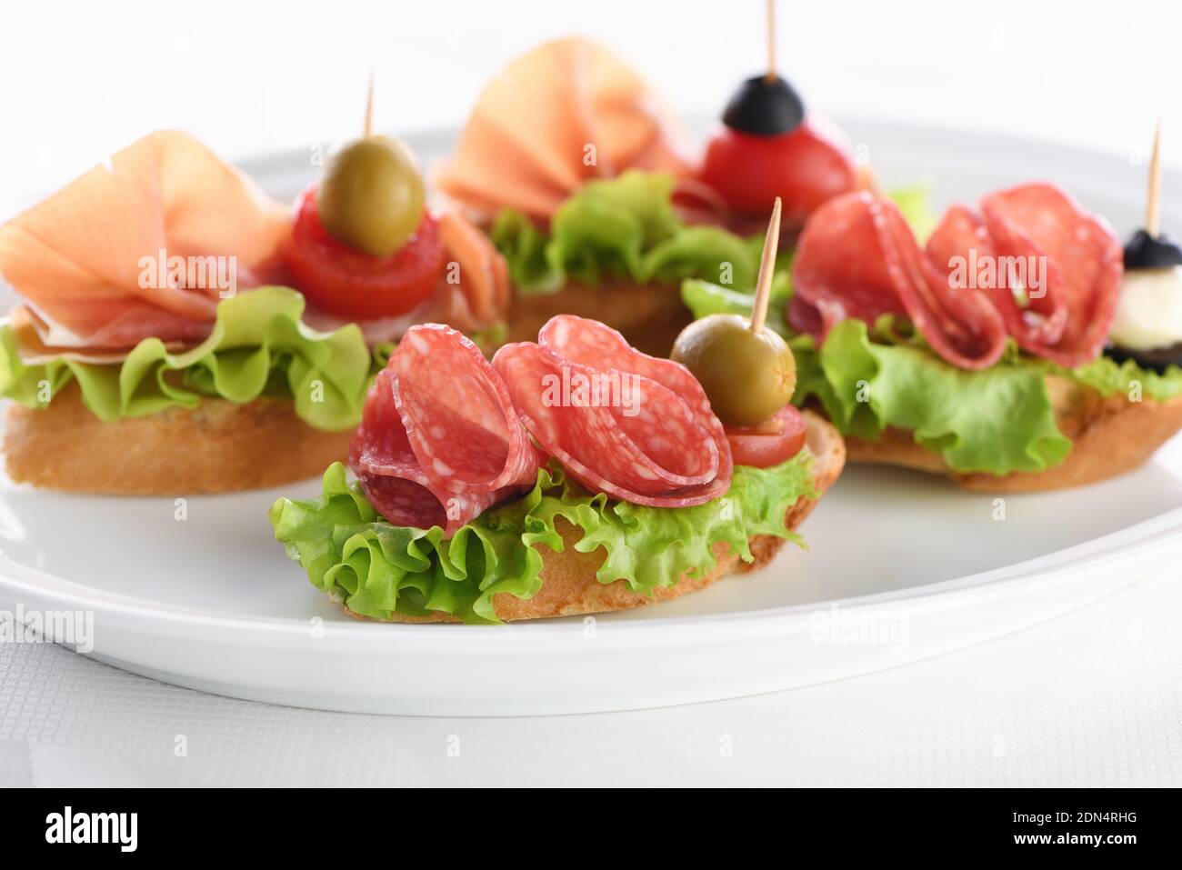 Tender baguette canapes with Leaf lettuce, salami or Parma ham, tomatoes, mozzarella and olive. Delicacy assorted platter for at the party. Stock Photo