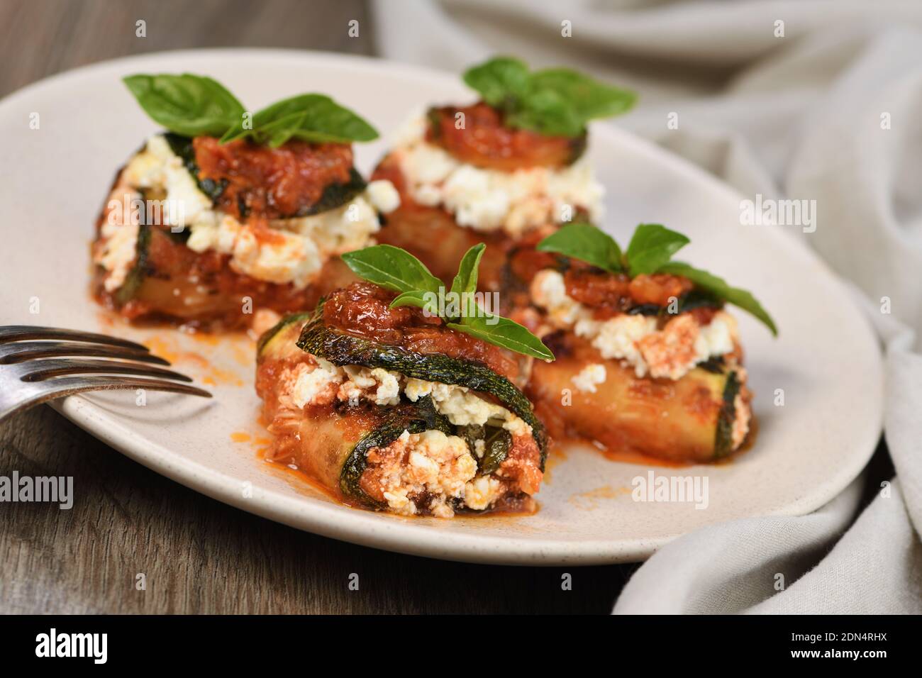 Baked zucchini rolls stuffed with ricotta and basil under tomatoonion