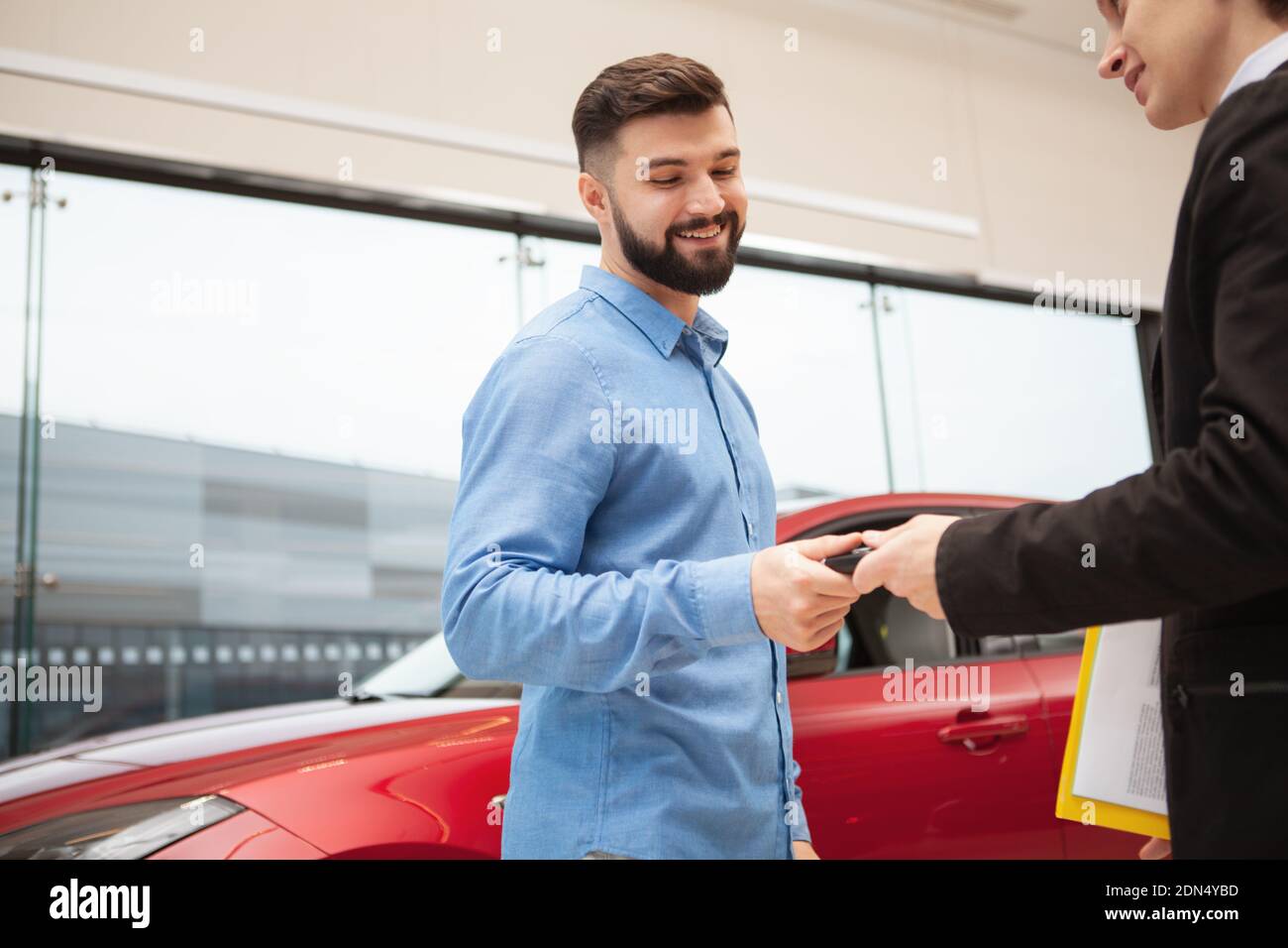 Low angle shot of a handsome bearded man receiving keys to his new car ...