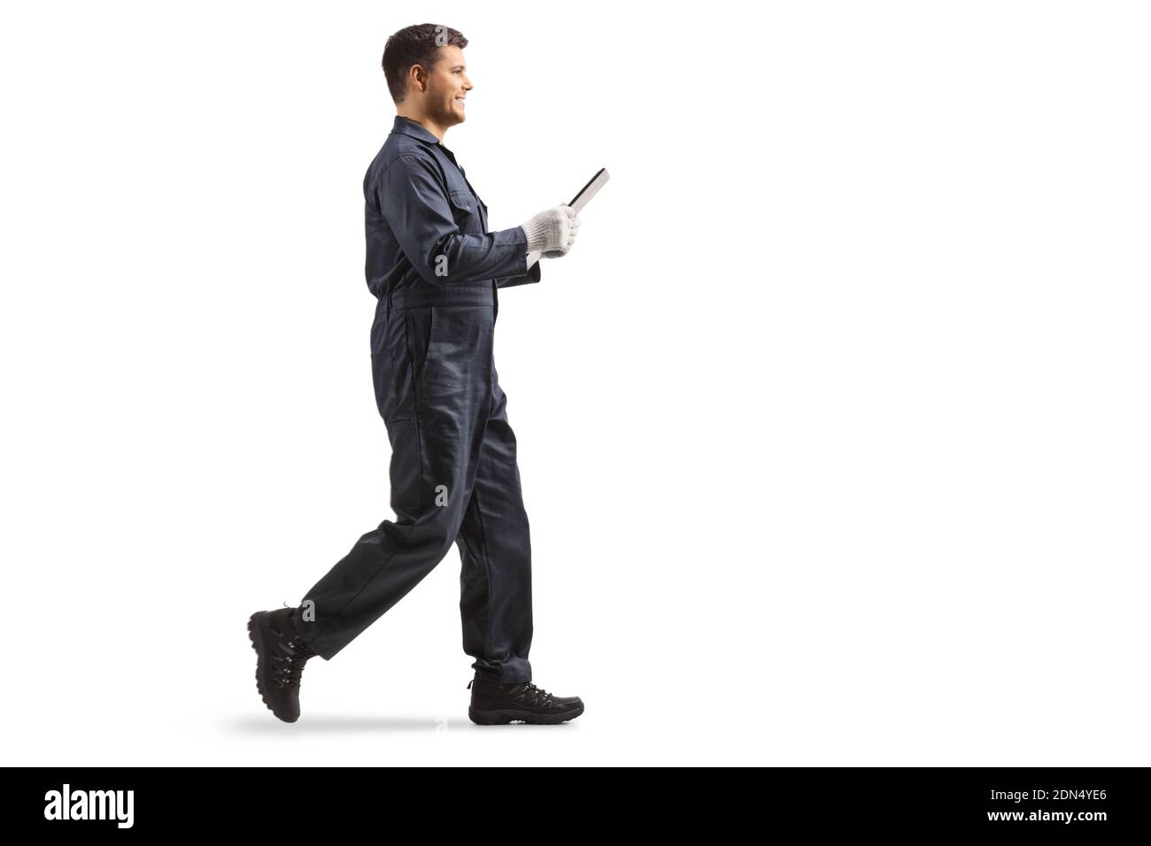 Full length profile shot of a young male worker in an overall uniform holding a clipboard and walking isolated on white background Stock Photo