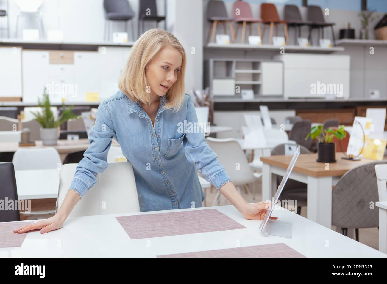 Charming young woman choosing furniture to buy for her new home. Lovely