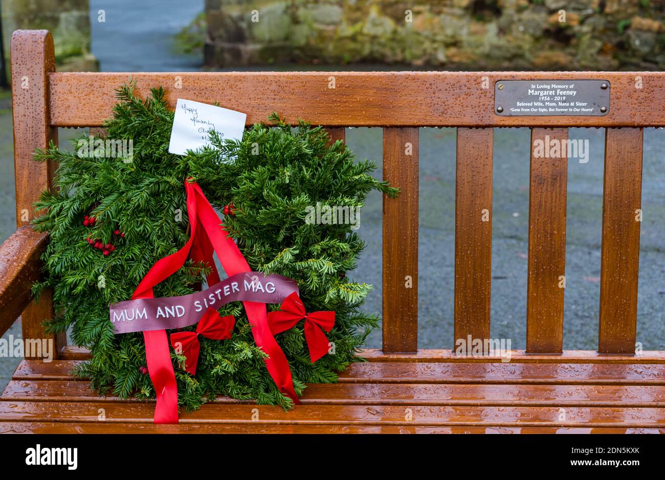 Commemorative wet wooden bench in the rain with Christmas wreath to remember a the death of a mother and sister relative, Scotland, United Kingdom Stock Photo