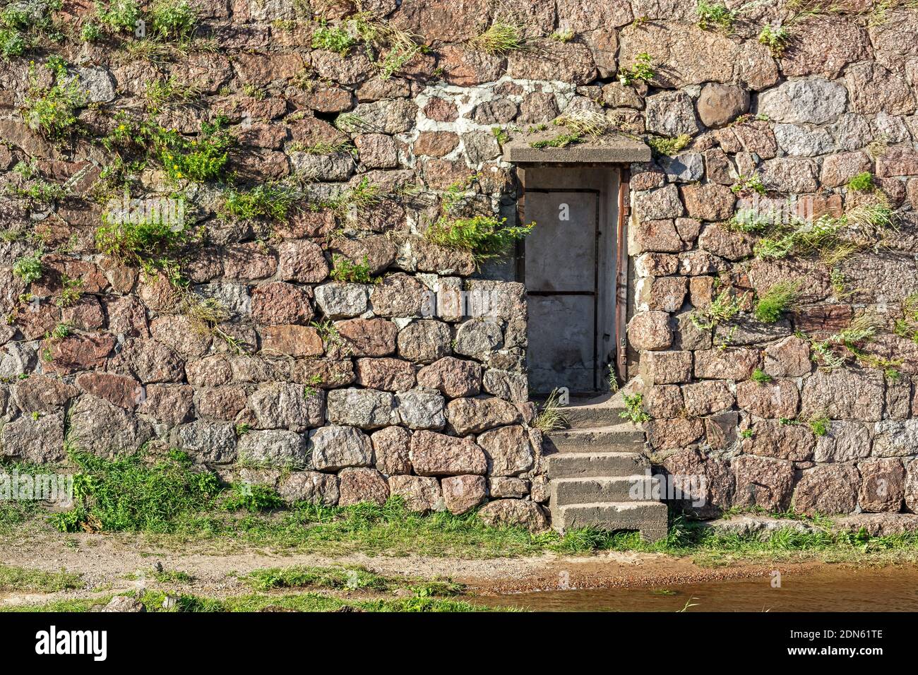 Door in the stone wall of the old fortress with stone steps leading to the river bank. Stock Photo