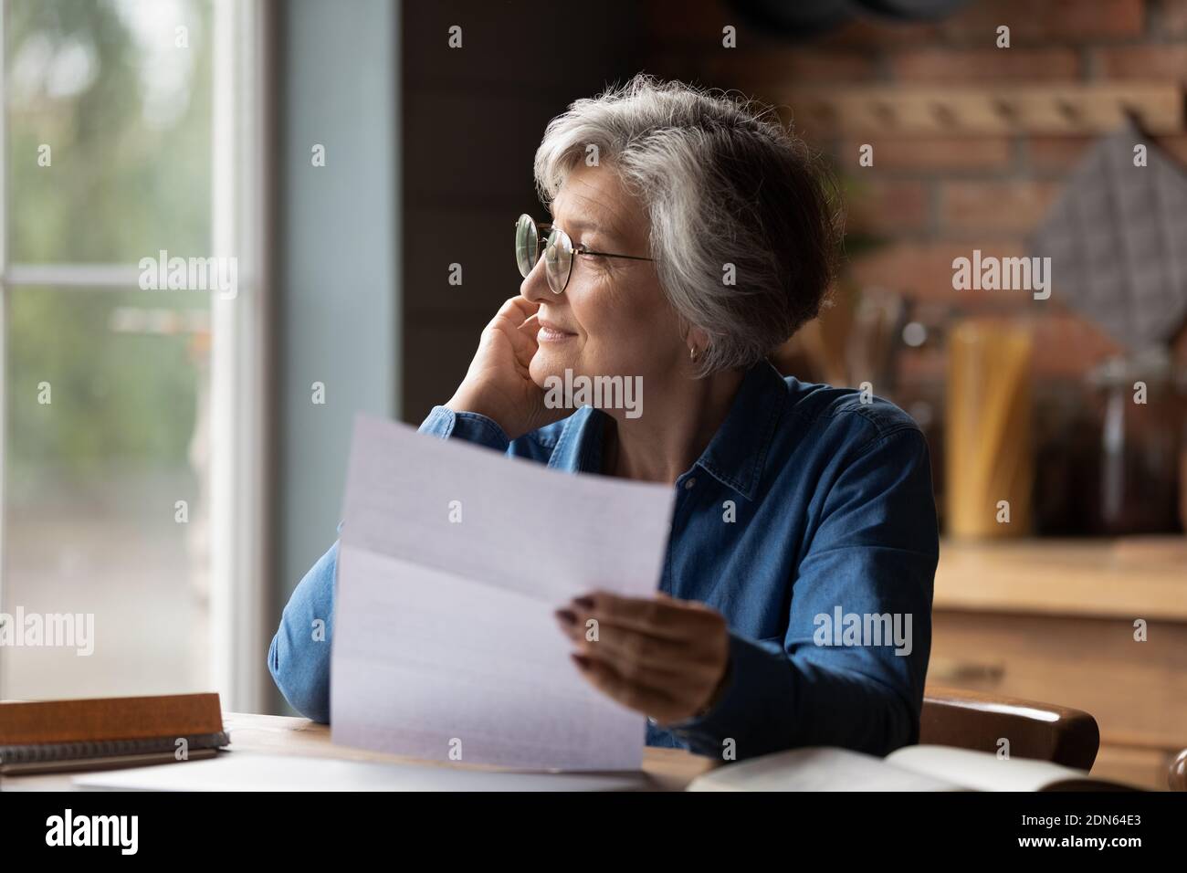 Thoughtful middle aged senior woman in eyeglasses holding paper document. Stock Photo