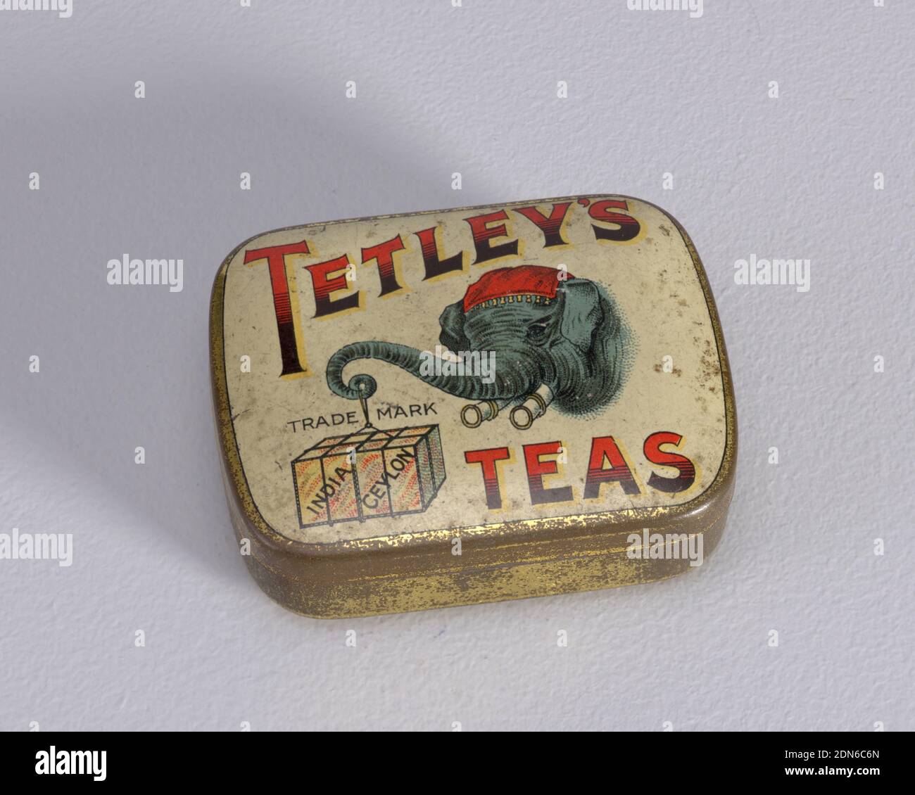 Advertisement for 'Tetley's Teas', Plated tin, enamel, Rectangular, rounded corners, with transfer printed decoration on lid, inscribed 'Tetley's Teas' in large red and black type-face, highlighted in yellow, featuring central image of blue elephant's head with red kerchief, elephant holds at end of curled trunk box on a string, box inscribed 'Indian Ceylon,' above box inscription reads 'Trade Mark,' all on off-white ground, edges, sides and underside gold. Lid hinged at back. Striker on underside., late 19th century, containers, Decorative Arts, Matchsafe Stock Photo