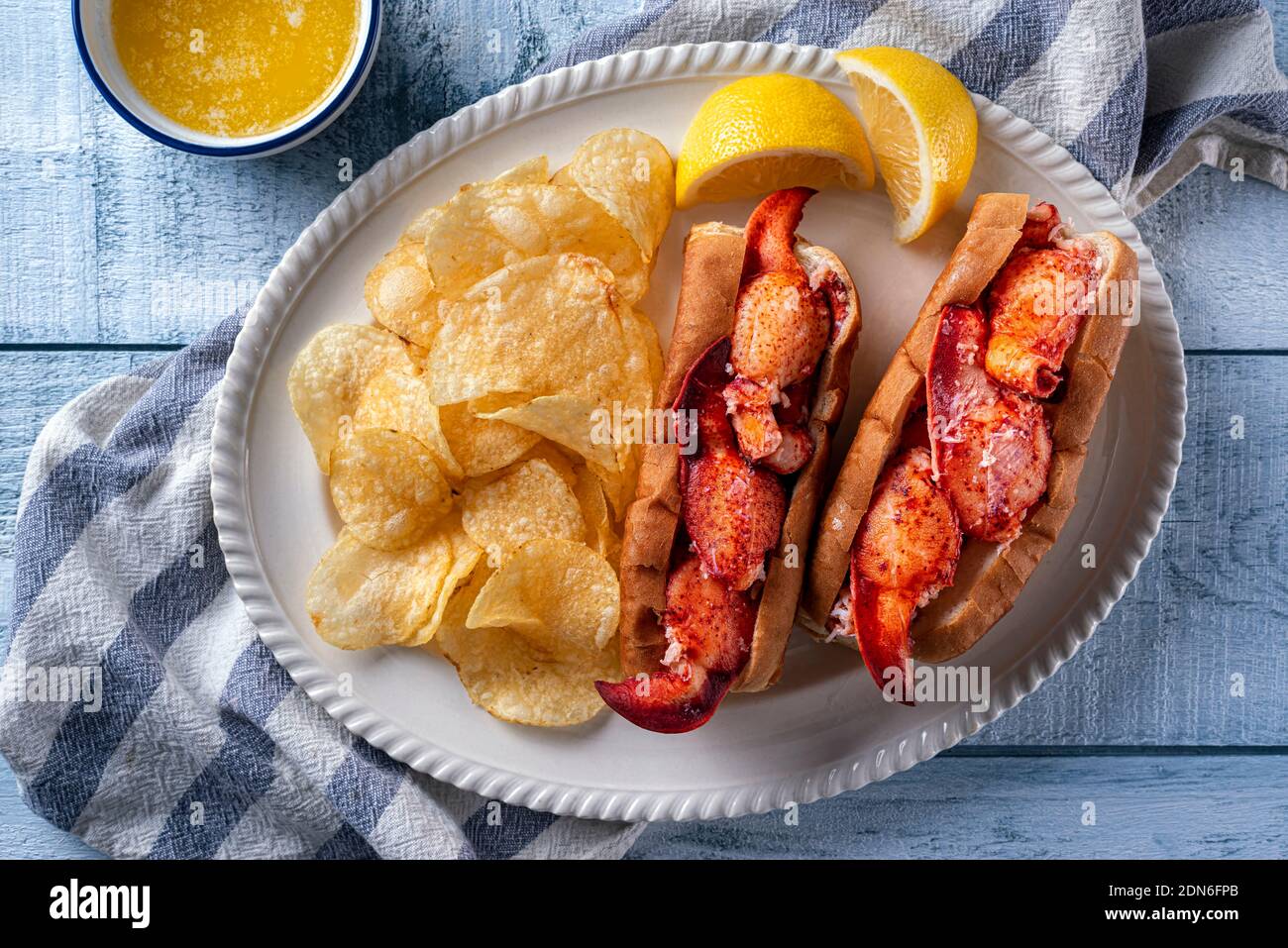 Delicious New England style lobster rolls with potato chips and melted butter on a wood table top, Stock Photo