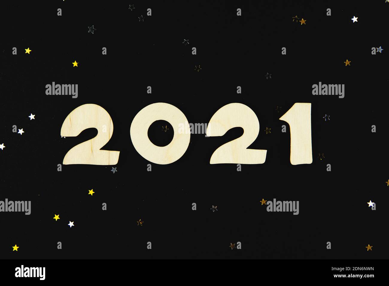 Wooden numbers 2021 on a black background with yellow and gray glitter stars. Stock Photo
