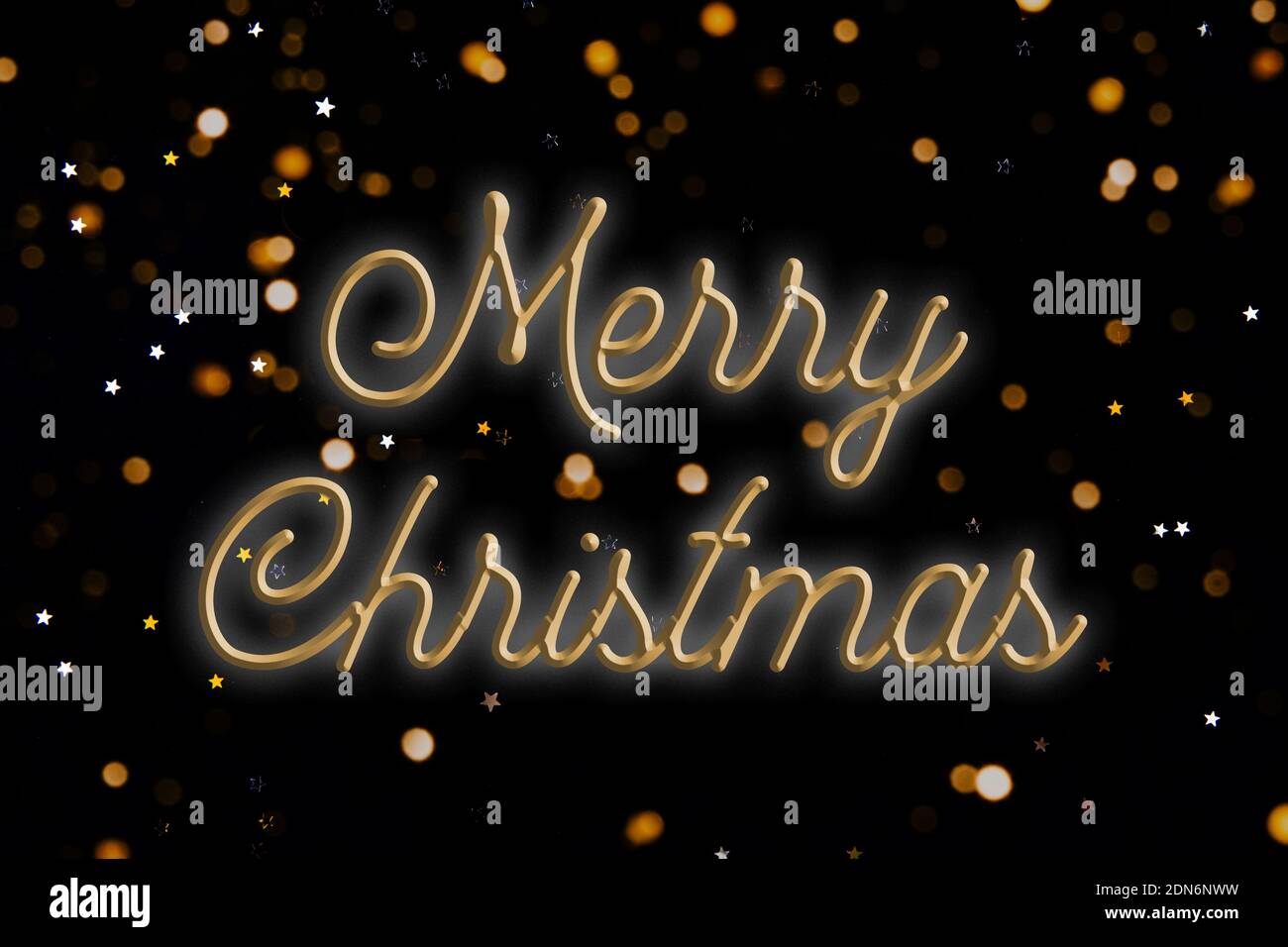Words MERRY CHRISTMAS on a black background. Christmas greeting card with blurred bokeh lights and small stars. Stock Photo