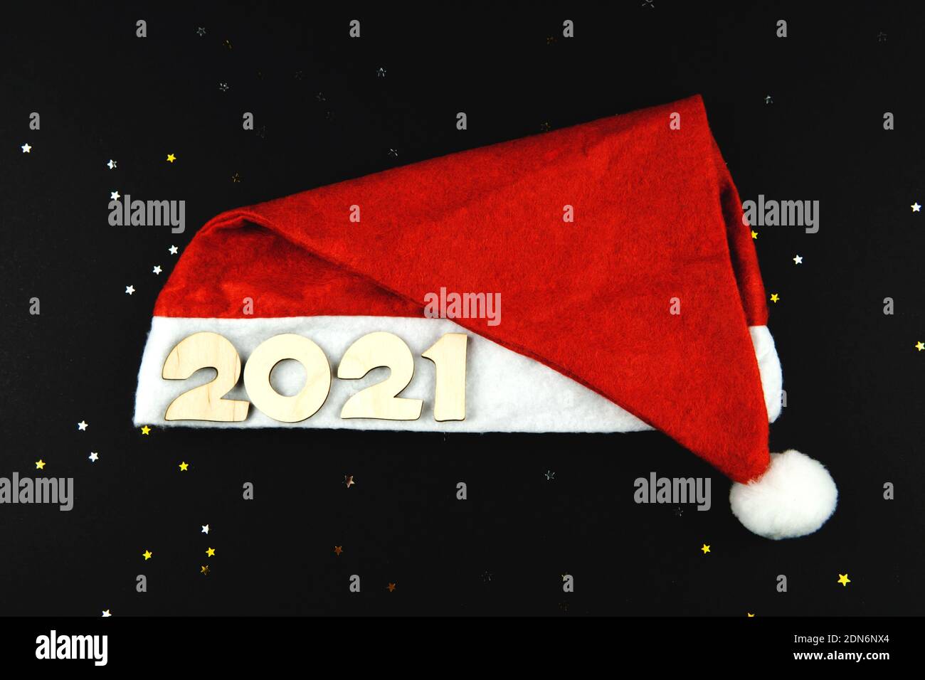 Wooden numbers 2021 on a red Santa hat on a black background with yellow and gray glitter stars. Stock Photo