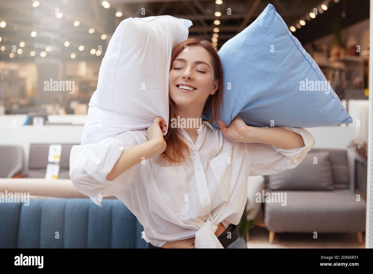 Lovely woman smiling joyfully while shopping for bedding at furniture store. Woman holding pillows, smiling with eyes shut Stock Photo