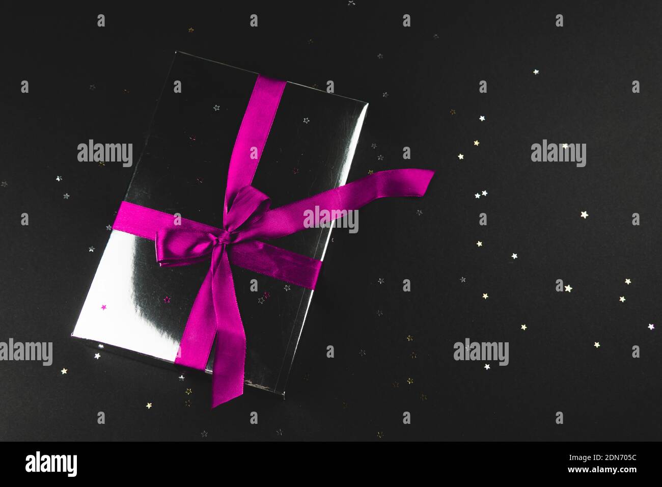 Gift box with a pink bow on a black background with small glitter stars. Holiday concept. Close up, flat lay, place for text. Stock Photo