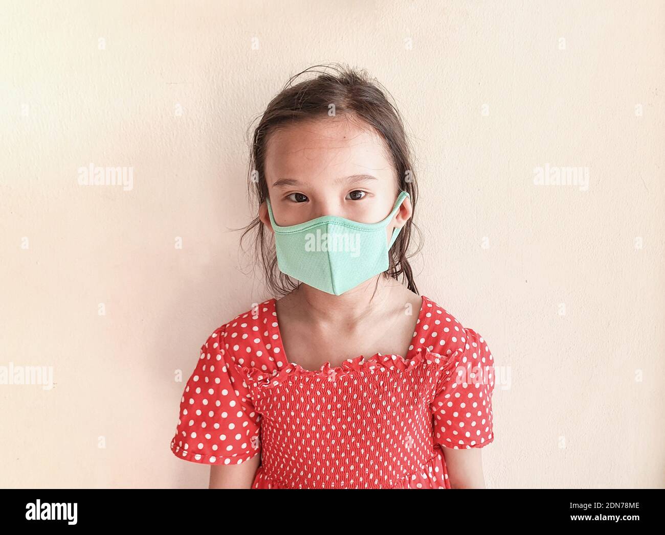 Close Up Of Asian Child Girl Wear Mask To Protect Against Viruses. Isolated On Cream Background Stock Photo