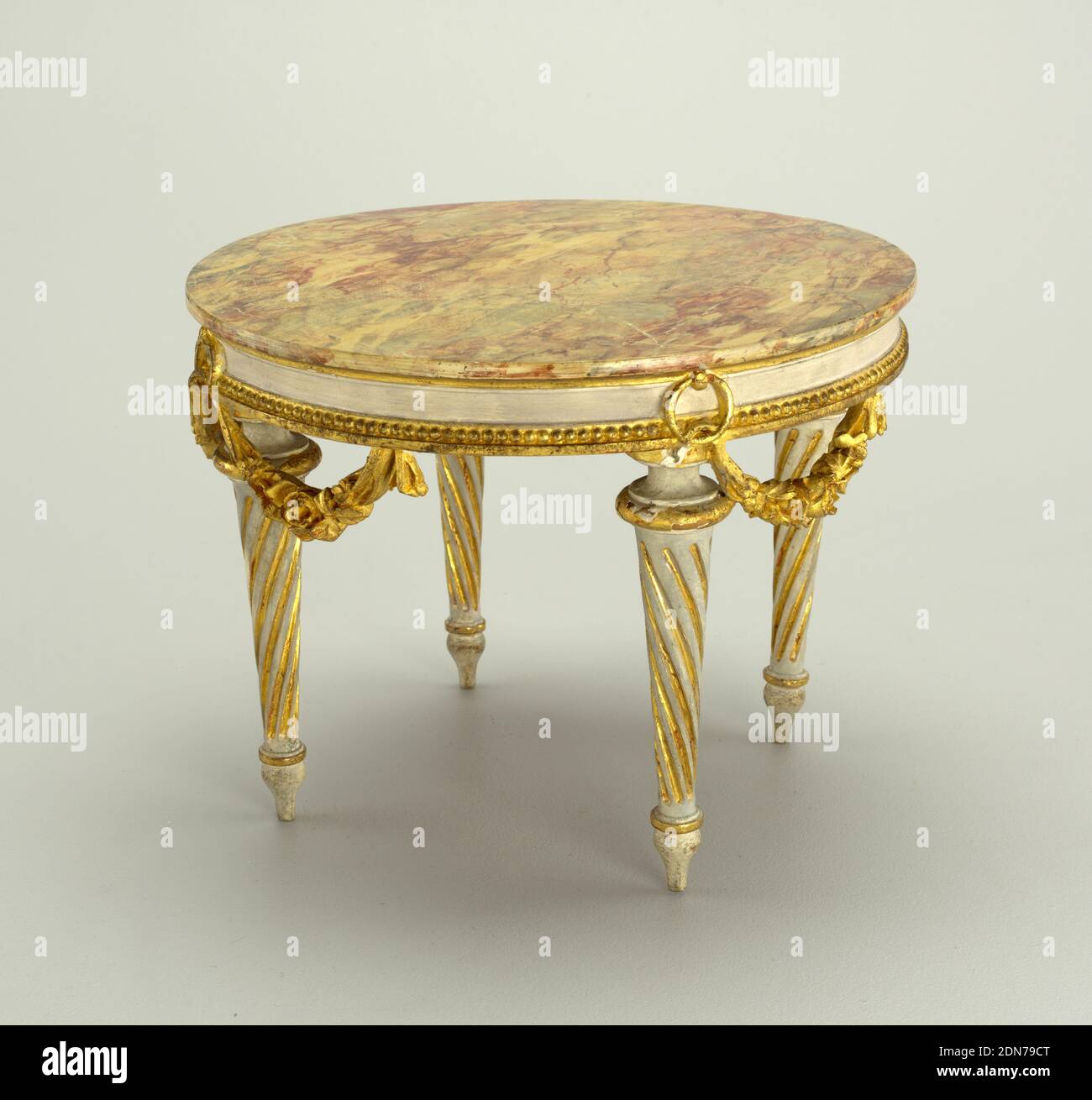 table, wood, carved, painted, gilded, Miniature table made of chestnut with a near circular top marbleized and carved in one piece with frieze rail which has beading on lower edge and free hanging flower garlands suspended by rings. Four tapering, spirally fluted legs terminating in baluster feet. Painted grayish white and gilt in parts., France, late 18th century, miniatures, Decorative Arts, Miniature, Miniature Stock Photo