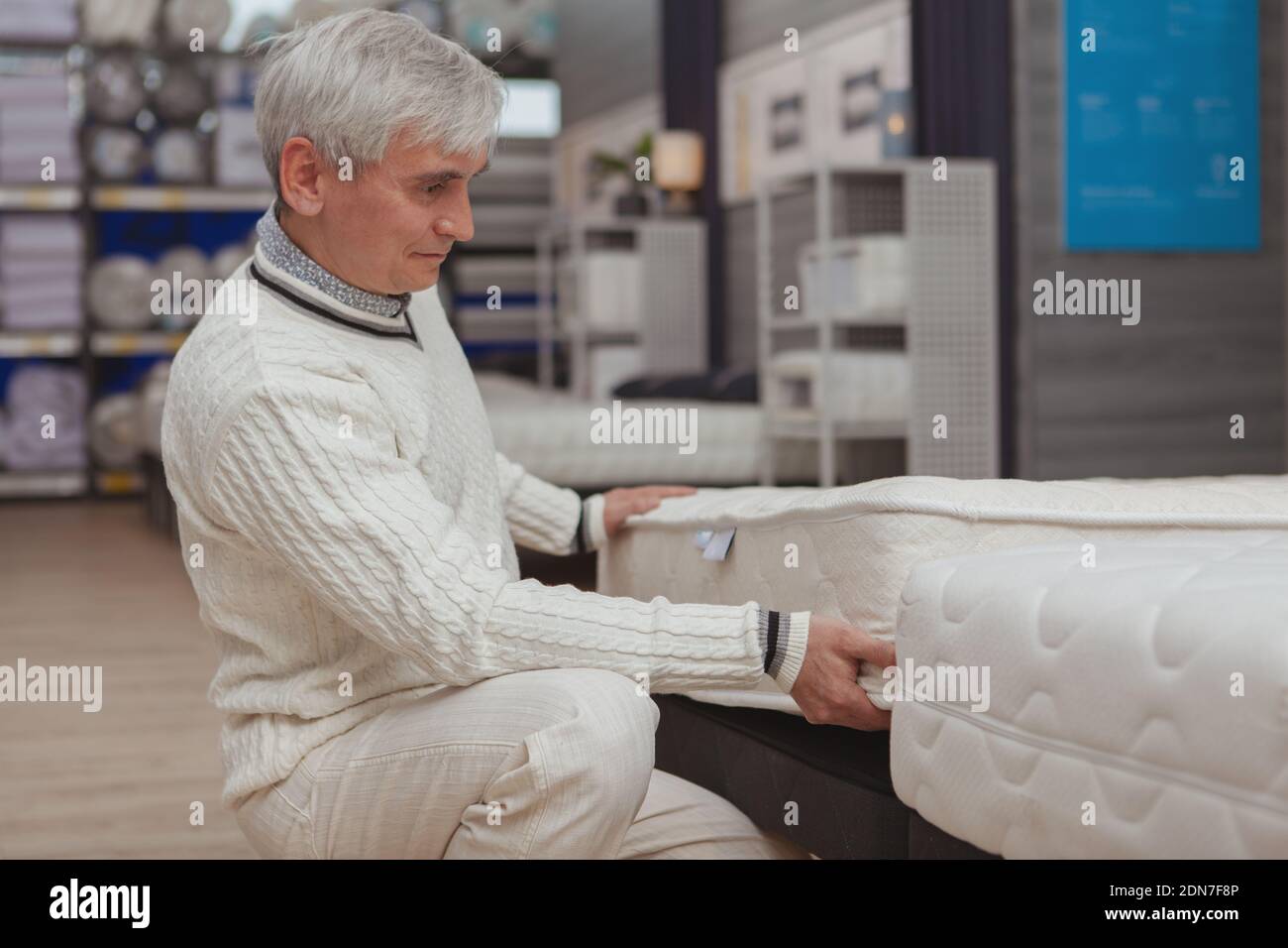 Senior male customer trying orthopedic mattress, shopping at furniture