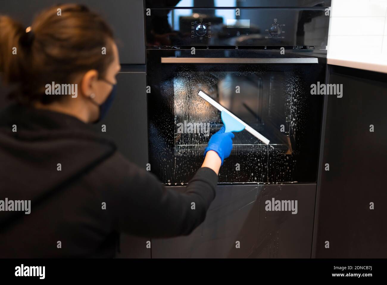 Woman washing the oven. Process of cleaning oven glass with water squeegee Stock Photo