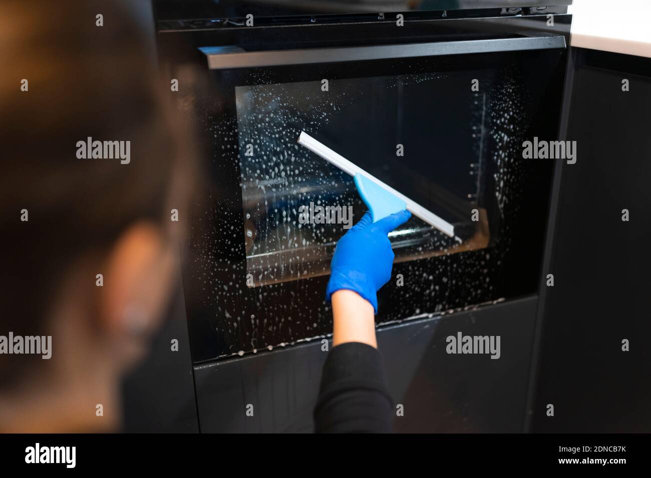 Woman washing the oven. Process of cleaning oven glass with water squeegee Stock Photo