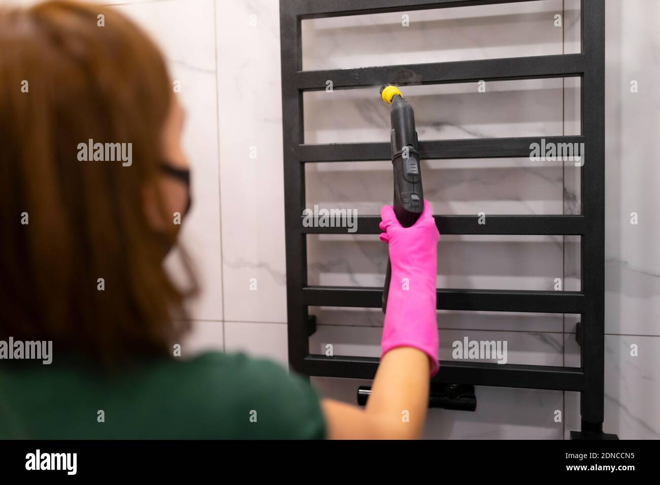 Woman doing steam cleaning of bathroom towel radiator. Heated towel ...