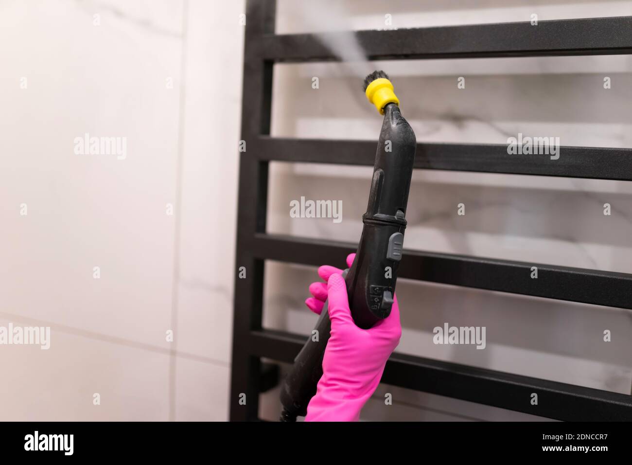 Woman doing steam cleaning of bathroom towel radiator. Heated towel ...