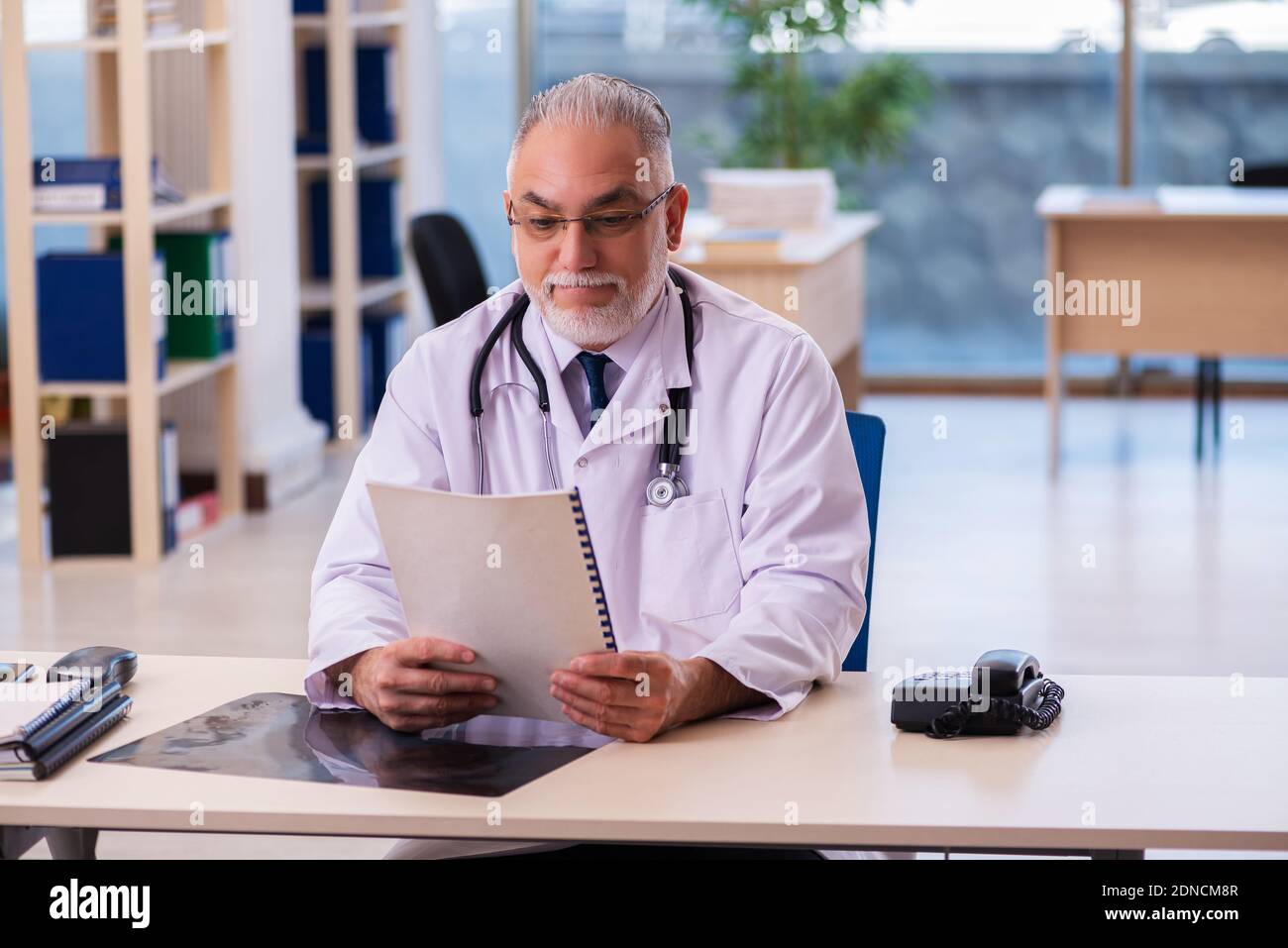 Old doctor taking notes in the clinic Stock Photo